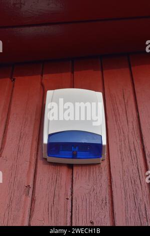 An der Wand montiertes blaues Sicherheitsalarm Sirene Stroboskop, Umkreiswarnung Notfallsystem Einheit, große vertikale Nahaufnahme, roter Holzbrett Hintergrund Stockfoto