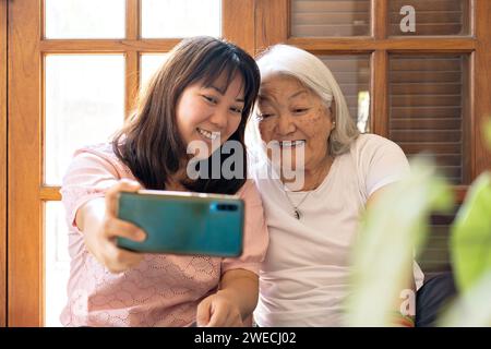 Liebende Tochter, die Selfie mit dem Handy macht, mit der Mutter zu Hause. Japanische Familie. Stockfoto