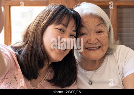 Japanische ältere Frau mit weißen Haaren und lächelnder Tochter, die ein Selfie macht Stockfoto