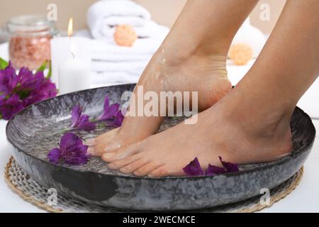 Frau, die Wasser auf ihre Füße gießt, in einer Schüssel auf dem Boden, Nahaufnahme. Spa-Behandlung Stockfoto