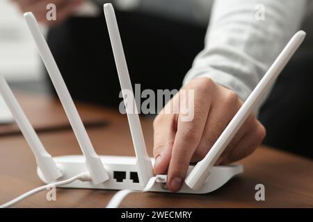 Mann, der Kabel in den WLAN-Router an einem Holztisch drinnen steckt, Nahaufnahme Stockfoto