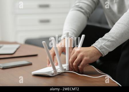 Mann, der Kabel in den WLAN-Router an einem Holztisch drinnen steckt, Nahaufnahme Stockfoto