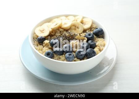 Leckeres Haferflocken mit Bananen, Heidelbeeren und Chiasamen, serviert in einer Schüssel auf weißem Holztisch Stockfoto
