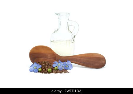 Holzlöffel gefüllt mit kleinen braunen Leinsamen und einer blauen Leinpflanze blüht neben Leinöl in Glasdekanter isoliert auf weißem Hintergrund Stockfoto