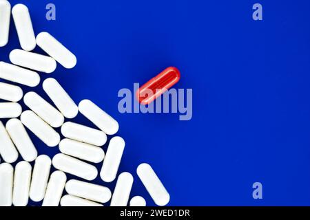 Große Anzahl weißer Pillen auf einer blauen Oberfläche verstreut, unter den weißen Pillen eine einzelne rote Pille, die den Fokus symbolisch für Einzigartigkeit o darstellt Stockfoto