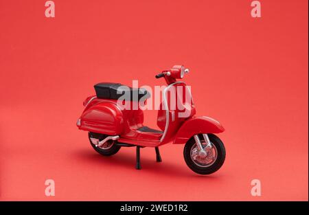 Foto einer alten Miniatur-Vespa, die auch Roller genannt wird. Fotografiert mit rotem Hintergrund, um das rote Vespa-Objekt zu isolieren Stockfoto