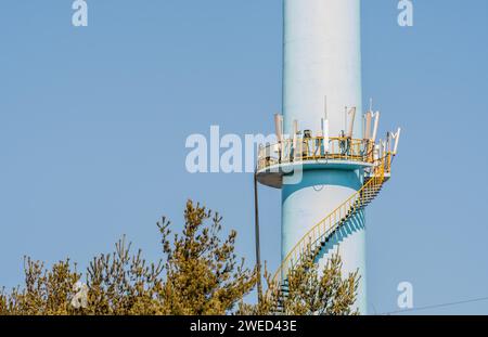 Nahaufnahme einer Wendeltreppe, die zu einer Funkübertragung auf einer hohen Betonsäule mit blauem Himmel im Hintergrund führt Stockfoto