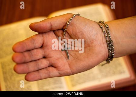 Die Hand hält ein kleines Kruzifix mit einer offenen Bibel auf dem Rücken Stockfoto