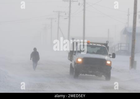 Inupiaq man läuft eine Straße im Dorf Kaktovik während eines Schneesturms entlang, während ein Lastwagen vorbeifährt, Barter Island, 1002 Gebiet des Arctic National Wil Stockfoto