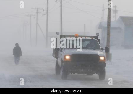 Inupiaq man läuft eine Straße im Dorf Kaktovik während eines Schneesturms entlang, während ein Lastwagen vorbeifährt, Barter Island, 1002 Gebiet des Arctic National Wil Stockfoto