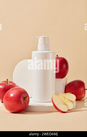 Vor beigefarbenem Hintergrund sind einige weiße Podeste, Äpfel und eine Flasche ohne Etikett angeordnet. Apfel (Malus domestica) ist reich an Vitamin C Stockfoto