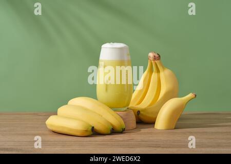 Ein Glas Bananensaft auf einem hölzernen Podium, dekoriert mit Bananenbündeln. Bananen enthalten reichlich Vitamin A, das stumpfsinnige s wiederherstellt Stockfoto