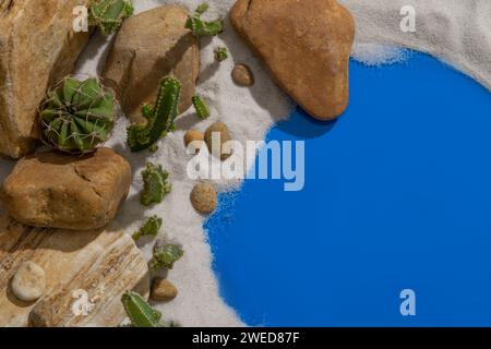 Vor sandigem Hintergrund sind mehrere Steine in verschiedenen Größen mit vielen grünen Kakteen neben einem See mit blauem Wasser angeordnet Stockfoto