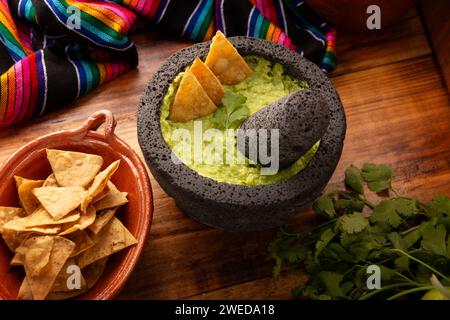 Guacamol. Avocado-Dip mit Tortilla-Chips, auch Nachos genannt, serviert in einer Schüssel aus vulkanischem Steinmörtel und Pistill, bekannt als Molcajete. Mexikanisch Stockfoto