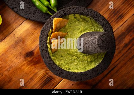 Guacamol. Avocado-Dip mit Tortilla-Chips, auch Nachos genannt, serviert in einer Schüssel aus vulkanischem Steinmörtel und Pistill, bekannt als Molcajete. Mexikanisch Stockfoto