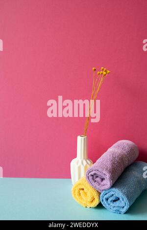 Stapel Duschtücher im Badezimmer mit einer Vase mit trockenen Blumen auf himmelblauem Regal. Pinkfarbener Wandhintergrund Stockfoto