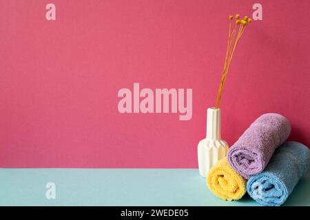 Stapel Duschtücher im Badezimmer mit einer Vase mit trockenen Blumen auf himmelblauem Regal. Pinkfarbener Wandhintergrund Stockfoto