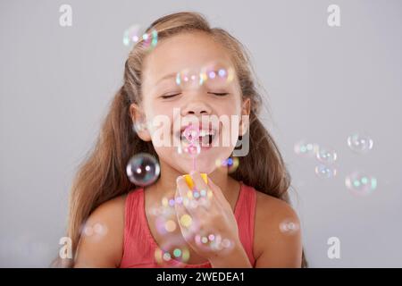 Glückliches, kleines Mädchen und Blasen im Studio von Spielzeug, süße und lustige Spiele für die Hand Augen Koordination. Kind, Augen geschlossen und mit dem Blasstab spielen Stockfoto