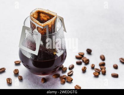 Ein Glas frisch gebrühten Tropfkaffee. Tropfkaffee-Beutel mit gemahlenem Kaffee zum Brühen in einem Glas Stockfoto