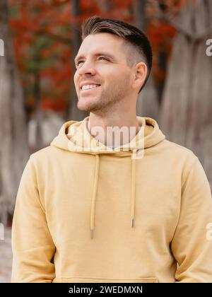 Schöner Mann im herbstlichen Wald. Porträt eines lächelnden kaukasiers in gelben Hoodies Stockfoto