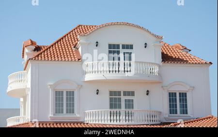 Ein modernes klassisches Haus, Luxusvilla, Villa mit weißen Wänden, Terrakotta-Ton, Keramikdach, großen Fenstern und halbkreisförmigen offenen Balkonen. Stockfoto