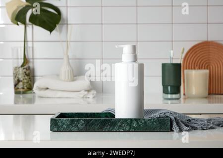 Vorderansicht der nicht etikettierten Kosmetikflasche auf Marmortablett mit grauem Handtuch, im Hintergrund sind Toilettenartikel, Schilfdiffusorflasche und kleine Topf. Stockfoto