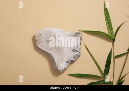 Produkt- und Werbekonzept für Werbung - ein kleiner grauer Stein als leeres Podium auf braunem Hintergrund mit grünen Bambusblättern. Leerraum für Co Stockfoto