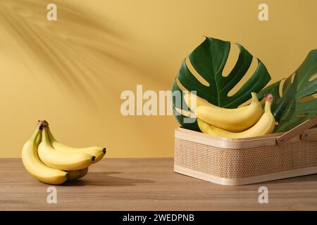 Hintergrund mit minimalistischem Stil für Produktmarkenpräsentation und Kopierraum - frische Bananen auf Bambuskorb mit Monsterablättern auf Holztisch o Stockfoto