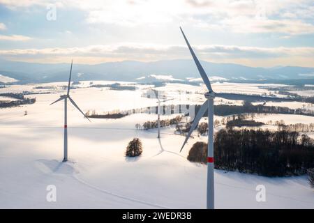 Windmühlen in winterlicher Weite bei Sonnenuntergang und Berge im Hintergrund. Windturbinen für grüne Energie. Stockfoto