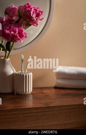 Ein kleines Eckbadezimmer mit rundem Spiegel, Baumwollhandtuch, Zahnbürste und Vase mit wunderschönen rosa Blumen. Szene für Werbung und Branding Stockfoto