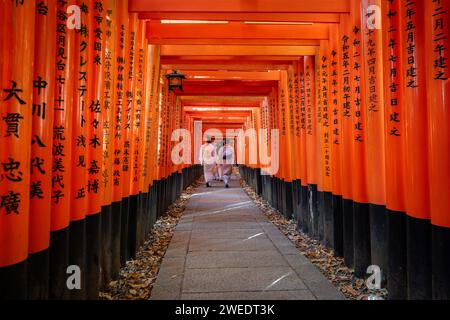 Frauen in traditionellen japanischen Kimonos gehen durch die roten Torii-Tore am Fushimi Inari-Schrein in Kyoto, Japan. Stockfoto