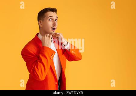 Fröhlicher extravaganter junger Mann in orangefarbener Jacke auf gelbem Hintergrund. Stockfoto