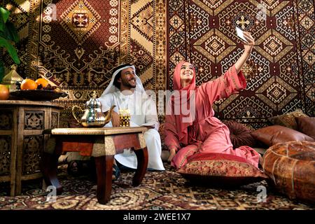 Ein junges Paar aus Emiraten verbringt Zeit in einem traditionellen arabischen Café. Mann und Frau tragen Kandura und Abaya aus Dubai, die sich miteinander unterhalten. Stockfoto