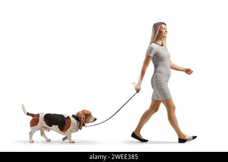 Profilaufnahme einer lässigen jungen Frau, die einen Basset-Hund auf einer Elektrode auf weißem Hintergrund führt Stockfoto