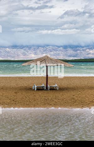 Nin, Kroatien - Schilfsonnenschatten am leeren Queen's Beach bei der mediterranen Stadt Nin am Ende des Sommers mit den Velebit Mountains im Hintergrund und Stockfoto