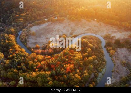 Der sich windende Fluss mitten in einem wunderschönen bunten Wald bei Sonnenaufgang. Luftlandschaft mit bunten Wäldern, kurvendem Fluss und hellem Sonnenschein im Herbst Stockfoto