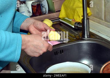 Eine Frau bereitet Essen zu. Sie schneidet geschälte Kartoffeln mit einem Messer in kleine Stücke. Stockfoto