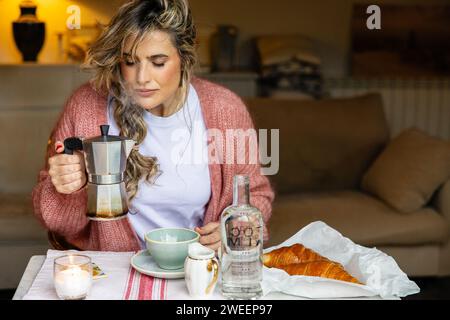 Eine gemütliche Morgenszene mit einer jungen Frau, die sich darauf vorbereitet, Kaffee aus einer Mokakanne zu gießen, mit einem frischen Croissant an der Seite. Stockfoto