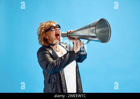 Reife Frau, Rentnerin in einem Trenchcoat aus Leder, der laut zu einem alten Megaphon schreien soll, um die Aufmerksamkeit der Menschen zu erregen. Stockfoto