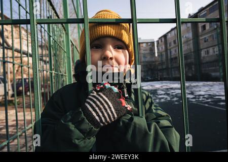 Porträt eines einsamen, traurigen Jungen hinter Gittern auf einem Spielplatz im Herbst Stockfoto