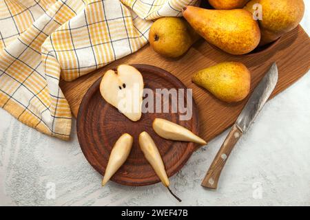Tonplatte mit Scheiben und der Hälfte reifer saftiger Birnenfrüchte, Korbkorb mit Birnen und gelbes Küchentuch auf Holzschneidebrett. Stockfoto