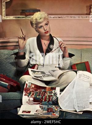 Die Schauspielerin Judy Holliday in einer Szene aus Born Yesterday (1950). In dieser klassischen romantischen Komödie spielt Holliday Billie Dawn, ein scheinbar unraffiniertes Ex-Chormädchen, das sich einer persönlichen Transformation unterzieht. Der Film verfolgt ihre Reise von der Naiveté zur Ermächtigung, hauptsächlich durch ihre Interaktionen mit einem Journalisten, gespielt von William Holden. Stockfoto
