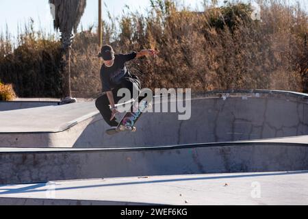 Anmutige Skate-Moves: Ein schicker Skater gleitet und springt mühelos in die pulsierende Energie des Skate-Parks Stockfoto