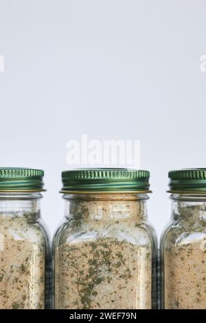 Drei Gläser mit Knoblauch, Salz und Kräutern, Gewürze und Gewürze stehen nebeneinander. Glasbehälter mit geschlossenem grünem Aluminiumdeckel auf grauem Hintergrund, Recycla Stockfoto