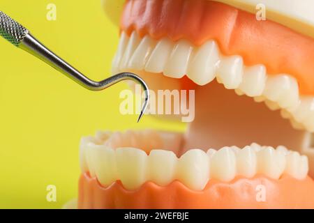 Zahninstrument auf gelbem Hintergrund in der Nähe eines Kiefermodells. Der Krankheitsbegriff und die zahnärztliche Behandlung in der Zahnheilkunde. Parodontitis und Gingivi Stockfoto