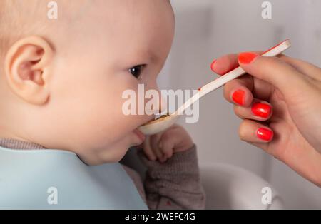 Eine Mutter füttert Brei von einem Löffel an einen kleinen Jungen, der 8 Monate alt ist. Säuglinge füttern. Nahaufnahme Stockfoto