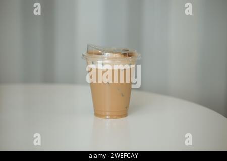 Eiscappuccino und Milchschaum in einem Plastikglas auf einem Holztisch in einem Café. Stockfoto