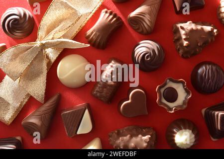 Auswahl an Schokoladenbonbons mit goldener Schleife in einer Ecke auf rotem Hintergrund. Draufsicht. Stockfoto