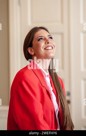 Eine junge Geschäftsfrau, die im roten Anzug sitzt und aufblickt Stockfoto