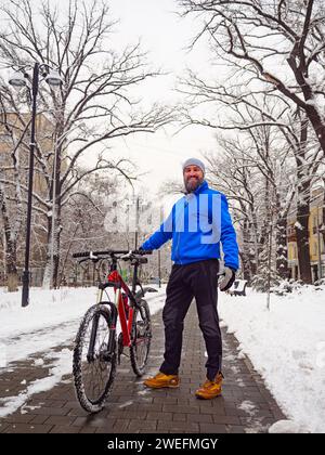 Lächelnder bärtiger Mann mit Fahrrad in einer Winterstadt. Aktiver Lebensstil. Stockfoto